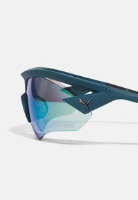 Lunettes de sport avec une monture en plastique bleu-vert, des verres réfléchissants dégradés dans des teintes de vert et de bleu, et un accent noir du logo Puma sur la branche.