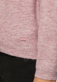 Jasnoróżowy sweter o żebrowej fakturze, z miękkiego materiału i małą metką z logo. Posiada luźny krój i długie rękawy.