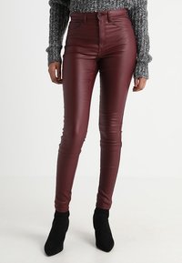 Pantalones de cuero sintético burdeos de talle alto con un ajuste ceñido, que presentan una textura suave y herrajes mínimos, combinados con botines negros.