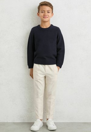 Laivastonsininen neulepaita, jossa resorireunaiset hihat, kermaan vivahtavat kapeat raidalliset housut ja valkoiset lenkkitossut. Yksinkertainen design, sopii rentoon pukeutumiseen.