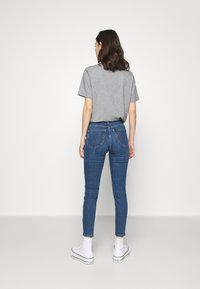 Blå denim skinny jeans med två bakfickor, i kombination med en grå t-shirt och vita sneakers. Enkelt design och figursydd stil.
