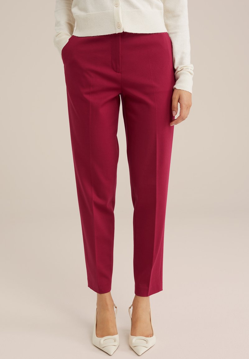 Magenta geschnittene Hose aus weichem Stoff, mit glatter Oberfläche und schrägen Taschen. Kombiniert mit weißen High Heels.