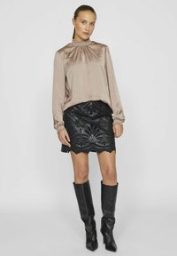 Silke beige bluse med lange ærmer og sammensnøret halsudskæring, parret med en sort præget miniskørt med blomster mønstre og bølget kant.