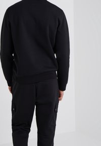 Svart sweatshirt med ribbad mudd och fåll, kombinerad med mörka joggingsbyxor som har sidfickor. Slät textur och avslappnad passform.