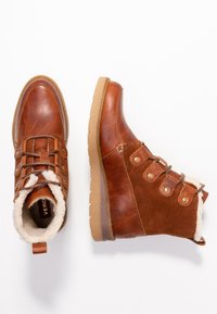 Botas de tobillo de cuero marrón y gamuza con forro de piel sintética, que presentan una puntera redonda, diseño con cordones y acentos en hardware en tono dorado.