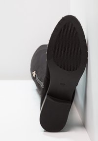 Botín negro de ante hasta el tobillo con cremallera lateral, textura suave, forma contorneada y suela de goma acanalada con pequeños studs metálicos.