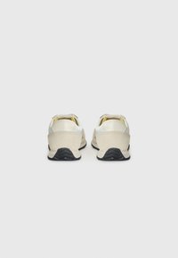 Chaussures décontractées avec une tige en cuir crème et des accents en daim beige, dotées d'une semelle texturée noire et de lacets jaunes à l'arrière.