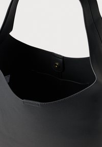 Black leather tote bag with a smooth texture, rounded shape, and an inner pocket secured by a gold snap button.