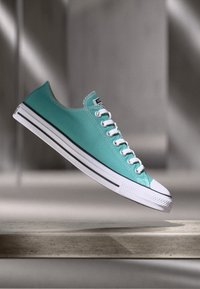 Turquoise canvas sneaker with white rubber sole and toe cap, featuring white laces and black stripes along the sole.