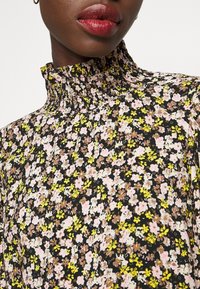 Bloemige blouse met een zwarte achtergrond en kleine roze, gele en bruine bloemen. Hoge gerimpelde kraag. Lichtgewicht stof met een zachte textuur.