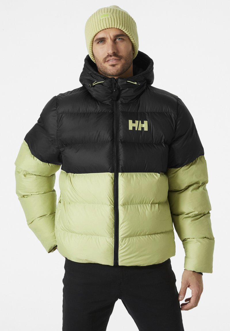 Chaqueta acolchada negra y verde claro con cremallera frontal, capucha y un logotipo prominente en el pecho. Acompañada de un gorro de punto a juego.