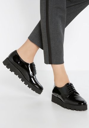 Chaussures vernies noires à lacets avec une épaisse semelle plateforme texturée. La chaussure présente des bords surélevés et un design à bout rond.