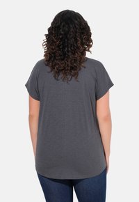 Graues T-Shirt mit kurzen Ärmeln und abgerundetem Saum, das eine glatte Textur und einen lockeren Schnitt aufweist, kombiniert mit dunkelblauen Jeans.
