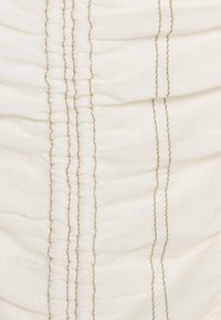 Krämfärgad tyg med vertikal rynkning, med kontrasterande beige sömmar som löper längs de samlade sömmarna. Slät textur.