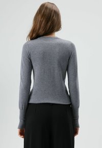 Grijze trui gemaakt van zacht materiaal, met lange mouwen en een ronde hals. De achterkant is glad zonder zichtbare sluitingen of patronen.