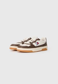 Baskets basses blanches et marron avec des lacets blancs, des semelles en gomme et des logos Tommy Jeans sur les côtés et les semelles intermédiaires.