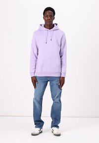 Light purple hoodie with a front pocket, adjustable drawstrings, and ribbed cuffs, paired with blue jeans and white sneakers.