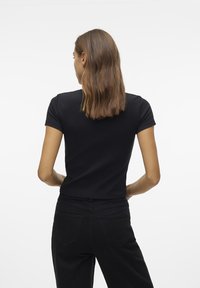 Svart tettsittende t-skjorte med korte ermer, sammen med svarte høyt midje jeans. Glatt tekstur, enkelt design og minimale detaljer.