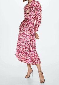 Robe longue à motif abstrait rose et blanc, avec un col, des manches longues et une jupe plissée. Associée à des talons argentés à brides.