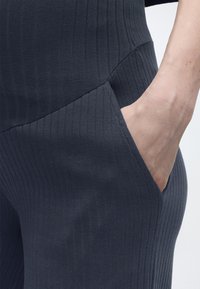 Χέρι στην τσέπη παντελονιού σκουρόχρωμου γκρι με ραβδώσεις, που δείχνει την υφή και τις ορατές ραφές.