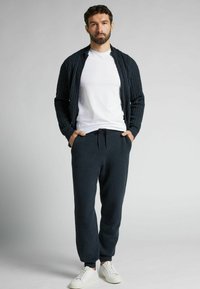 Granatowy kardigan w splot żakardowy na białej koszulce, w zestawieniu z ciemnymi spodniami dresowymi i białymi sneakersami. Teksturowany materiał, swobodny krój.