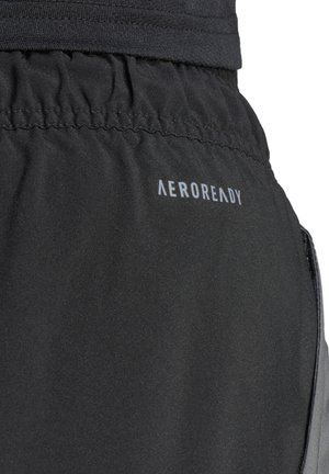 Zwarte sportshorts zijn gemaakt van een zachte, gladde stof en hebben een elastische tailleband en een reflecterende "AEROREADY"-logo aan de zijkant.