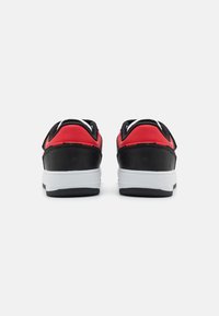 Svart og rød sneaker med overdel i teksturert skinn og mesh, polstret krage, hvit mellomsåle og gummisåle. Bakfra vises detaljene.