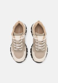 Baskets beige et crème en mesh et daim, bout rond, lacets blancs plats, semelle épaisse en caoutchouc noir, et nom de la marque sur la semelle intérieure.