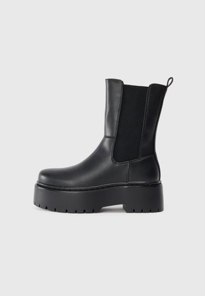 Black ankle boot made of smooth leather, featuring elastic side panels, a pull tab, and a chunky rubber sole with textured tread.