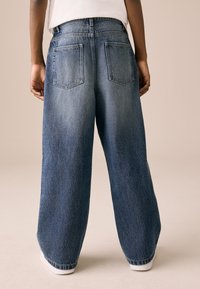 Laiade säärega keskmise tooniga teksapüksid kõrge vöökohaga, kahel tagataskul ja mansettidega ääred. Sile tekstuur, vabaaja stiil.