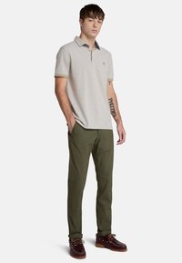 Ljust grå polo med krage, mörkblå detaljer, gröna byxor och vinröda skor med bruna sulor. Avslappnad passform, korta ärmar.