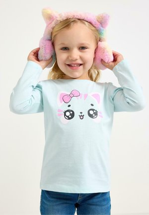 Vaaleansininen pitkähiha shirt , jossa on sarjakuvatyylinen kissan kasvot pinkillä rusetilla, yhdistetty värikkäisiin pörröisiin korvalappuihin. Lapsi hymyilee poseeratessaan.