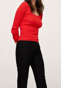 Rode geribbelde top met lange mouwen en een vierkante halslijn, gecombineerd met zwarte strakke broek. De stof heeft een zichtbare textuur en een nauwsluitend ontwerp.