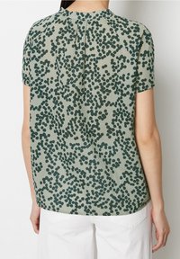 Blouse à manches courtes verte avec un motif à pois en vert foncé, dotée d'un col arrondi et d'un pli décoratif à l'arrière.