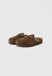 Καφέ σουέντ κλογκς με καμπυλωτή μύτη, μία λουρίδα διακοσμημένη με μεταλλική αγκράφα και υφασμένο φελλό στη σόλα. Λείο και απαλό φινίρισμα.