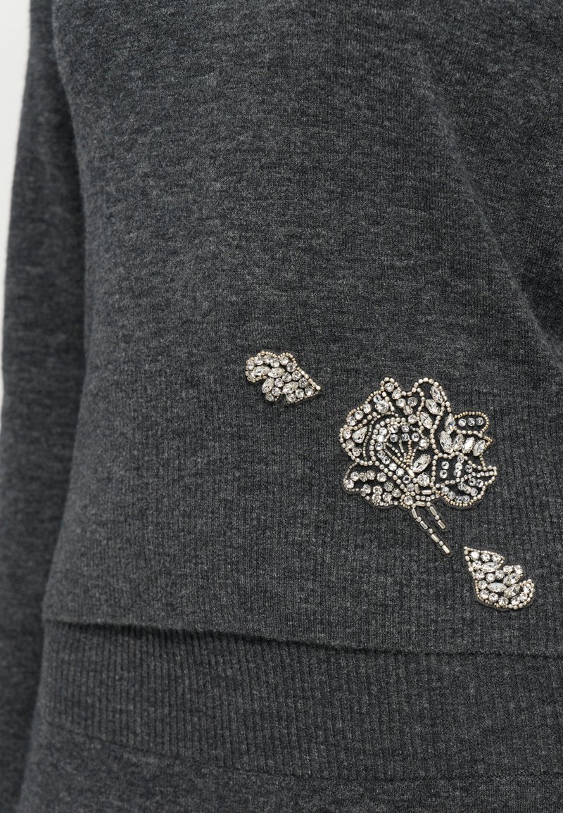 Tissu tricoté gris foncé avec un petit cluster décoratif complexe de strass en argent et en transparent en forme de fleur et de feuilles.
