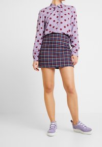 Lila prickig skjorta med knappar, matchad med en rutigt mini kjol i marinblått, rött och vitt. Kompletteras med ljuslila sneakers.