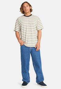 Gestreiftes T-Shirt mit kurzen Ärmeln in Creme und Blau, kombiniert mit lockeren blauen Jeans und schwarzen Sneakers. Einfacher runder Ausschnitt, normale Passform.