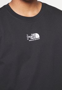 Camiseta de algodón negra con cuello redondo. Presenta un logo blanco que dice "THE NORTH FACE" y "NEVER STOP EXPLORING" en el pecho.