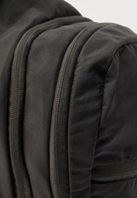 Gros plan sur un sac à dos en tissu noir montrant deux fermetures éclair verticales légèrement ouvertes et des sections rembourrées.