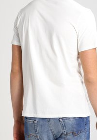 Vit bomullströja med korta ärmar, med en klassisk rundad halsringning och en slät yta. Bärs tillsammans med denimjeans.