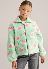 Giacca in pile verde con motivo floreale rosa, cerniera frontale e colletto. Caratterizzata da una vestibilità comoda e maniche leggermente imbottite.