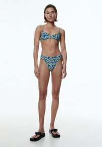 Bikini-set met bloemenpatroon in blauwe, groene en gele tinten. De bovenkant heeft verstelbare bandjes en een geplooid ontwerp, gecombineerd met bijpassende low-rise slipjes.