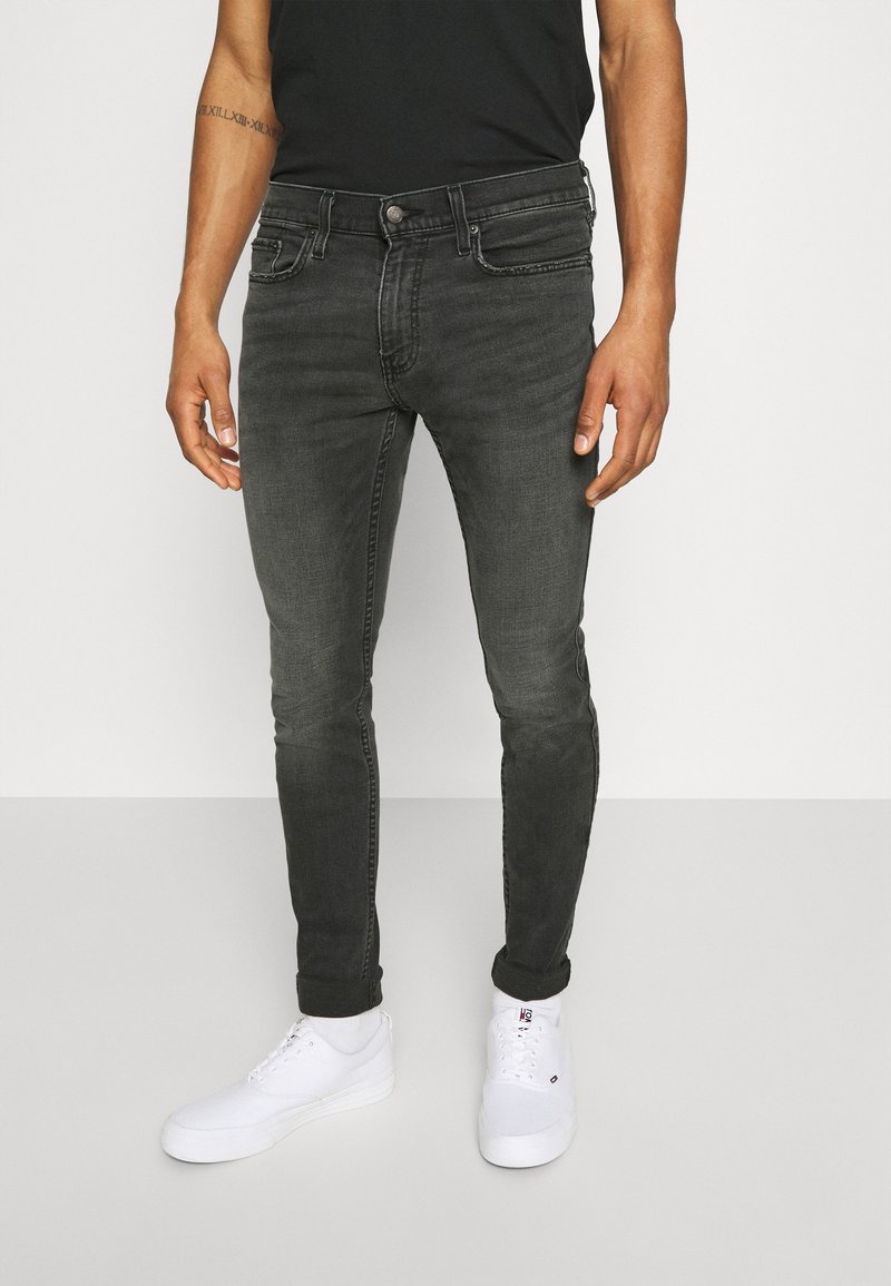 Slim fit jeans i mörkgrå denim, med en klassisk femficksdesign, subtila slitningar och en medelhög midja. Kombineras med vita sneakers.