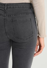 Jeans ajustados negros con una textura suave, que cuentan con un bolsillo trasero y costuras en contraste. La cinturilla es de talle alto y tiene presillas para el cinturón.