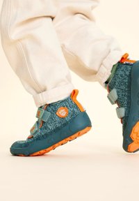 Scarpine per bambini in blu e verde con texture, dettagli arancioni e strap in Velcro, dotate di suola in gomma e un logo giocoso.