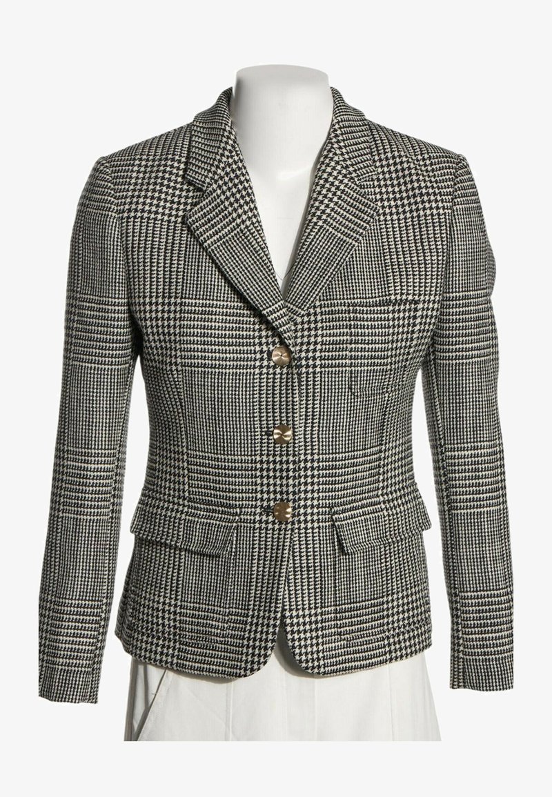 Veste ajustée à motif pied-de-poule noir et blanc avec trois boutons en métal, revers crantés et poches avant à rabat sur un mannequin blanc.