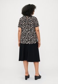 Blouse à motifs noir et crème avec des manches courtes, associée à une jupe noire jusqu'aux genoux. Présente un détail en forme de trou de serrure au dos.