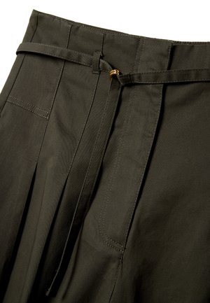 Dunkelgrüne, hoch taillierte Hose mit Falten, einem schmalen passenden Gürtel mit kleiner goldener Schnalle sowie sichtbaren Gürtelschlaufen und Nähten.