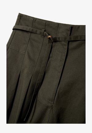 Donkergroene hoge taille broek met plooien, een smalle bijpassende riem met een kleine gouden gesp, en zichtbare riemlussen en stiknaden.